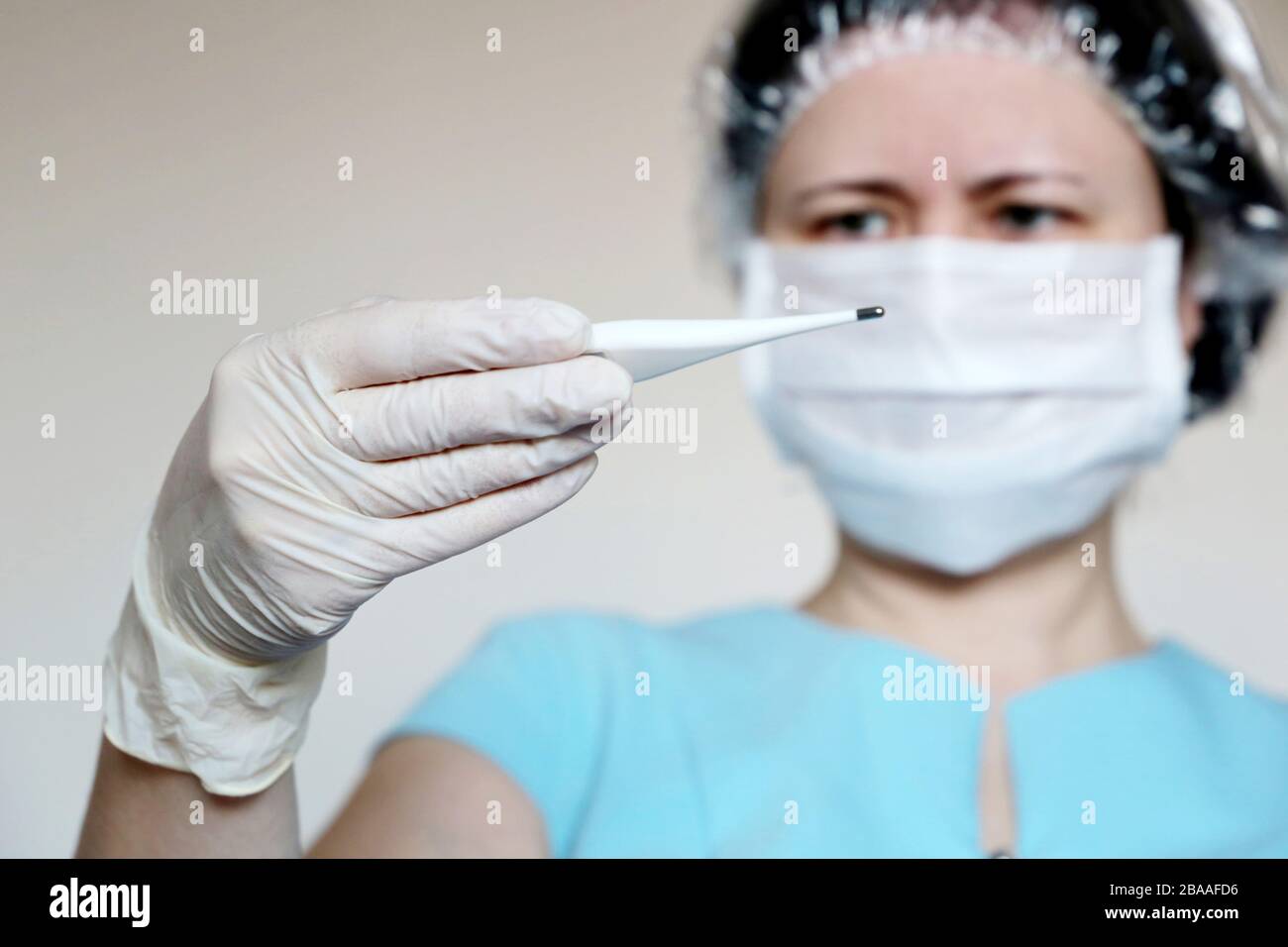 Síntomas del coronavirus, la mujer con máscara médica mide la temperatura corporal. El doctor mira el termómetro digital en su mano, el concepto de frío y gripe Foto de stock