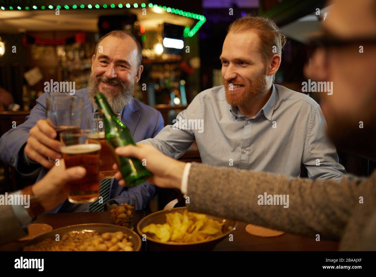 Felices hombres barbudos toastando con cerveza y divirtiéndose después del día de trabajo en el pub Foto de stock
