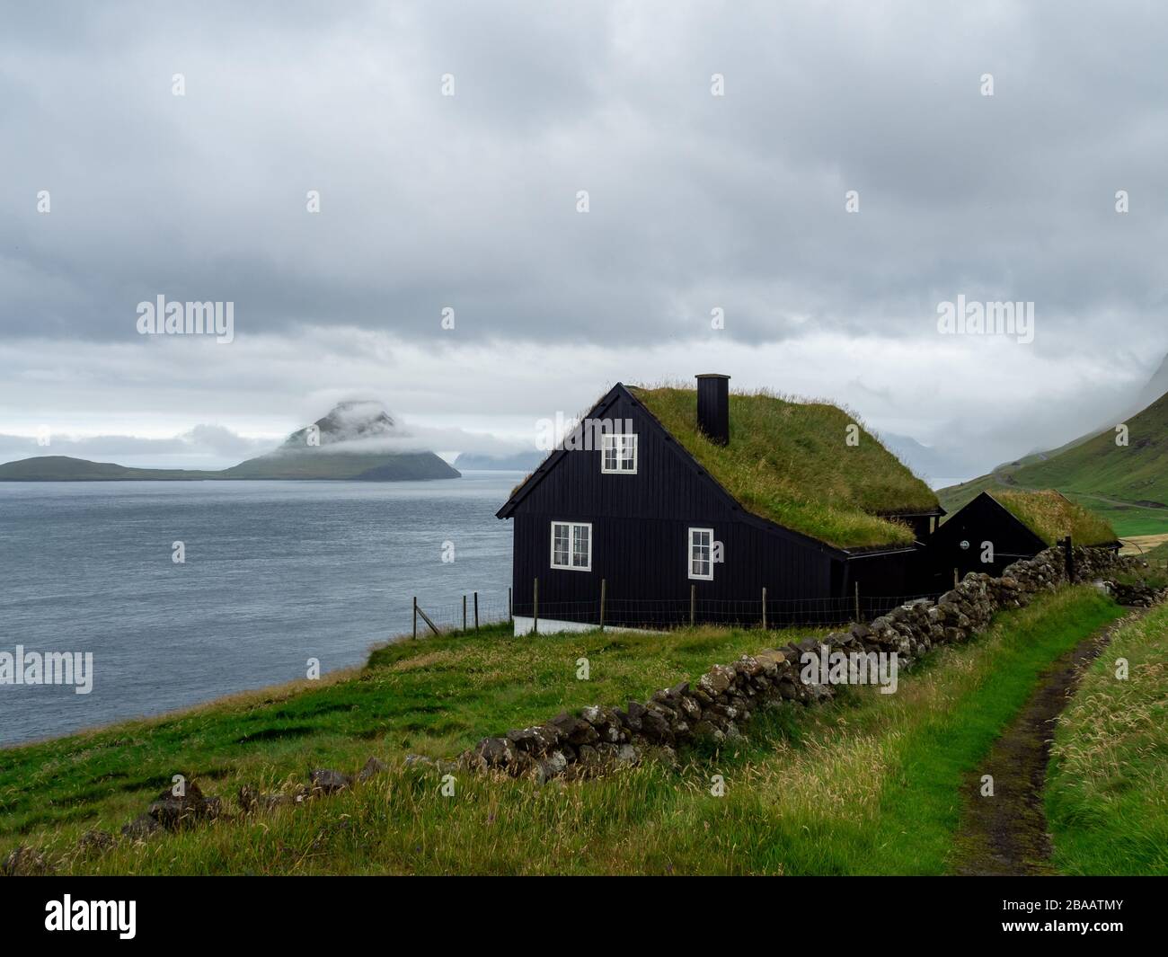Islas Feroe. Casa con techo de hierba en la ladera de la colina. Paisaje avelloso. Clima nublado. Foto de stock