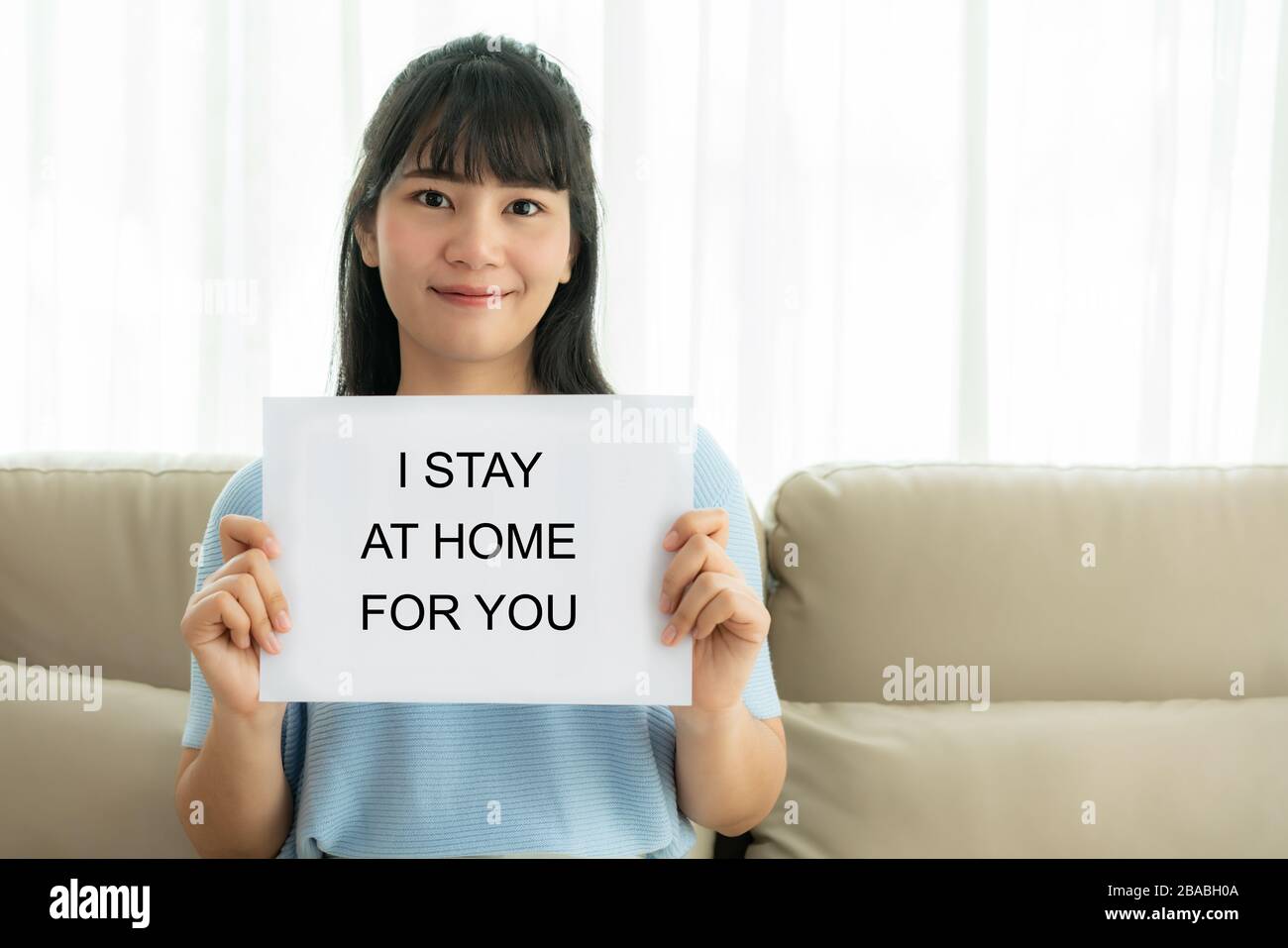 Mujer asiática sosteniendo hoja de papel con texto me alojo en casa para que usted anime al personal médico para proteger el virus y cuidar de su salud de COVID-1 Foto de stock