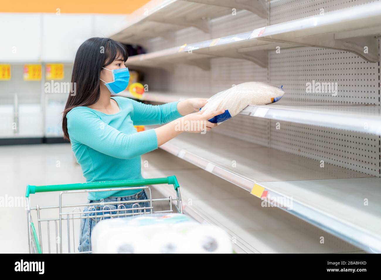 Mujer asiática recoger el último paquete de arroz en los estantes vacíos Supermarket en medio de COVID-19 coronavirus temores, compradores pánico compra y almacenamiento de papel higiénico pr Foto de stock