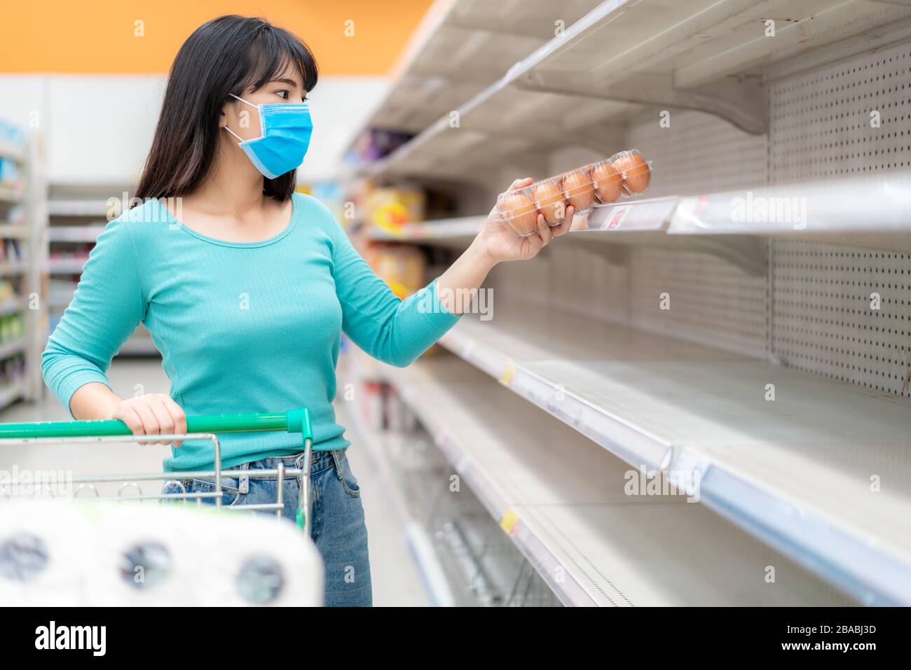 Mujer asiática recoger último paquete de huevos en los estantes vacíos de Supermarket en medio de COVID-19 coronavirus temores, compradores pánico compra y almacenamiento de papel higiénico pre Foto de stock