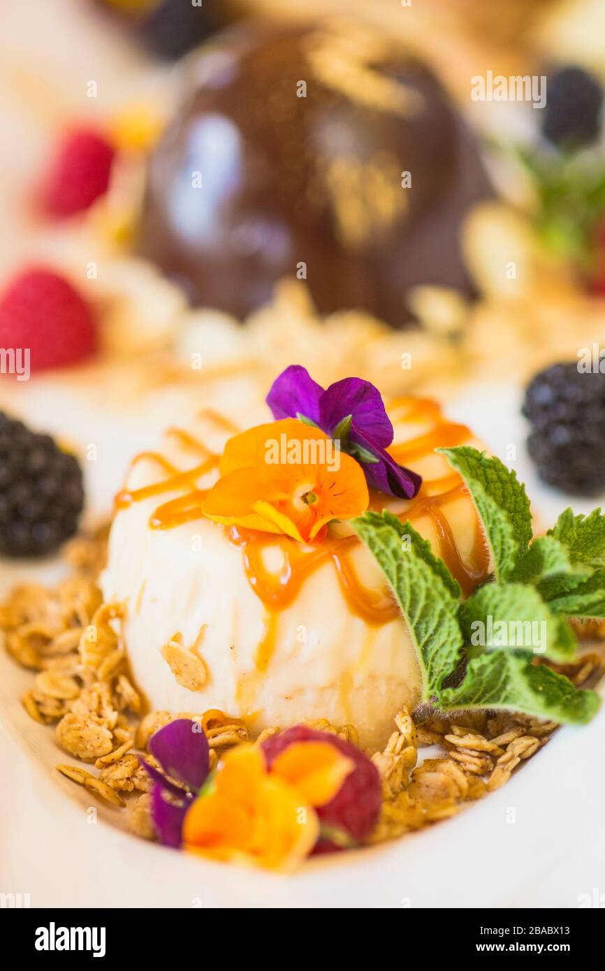 helado con salsa de caramelo y flores comestibles, plato de postre Foto de stock