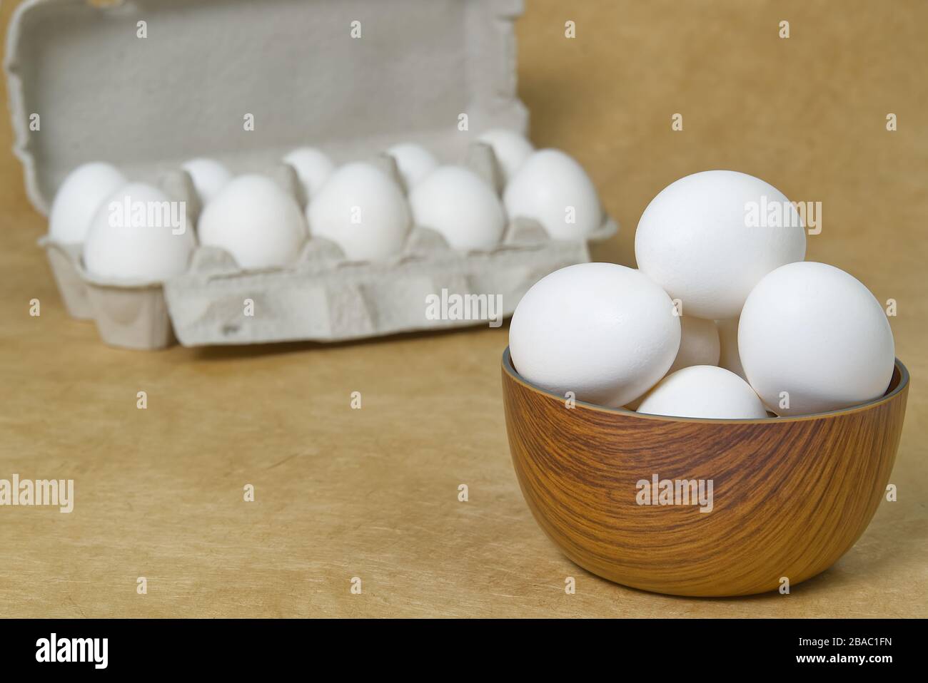 Huevos blancos aislados en un tazón de madera sobre fondo de textura beige Foto de stock