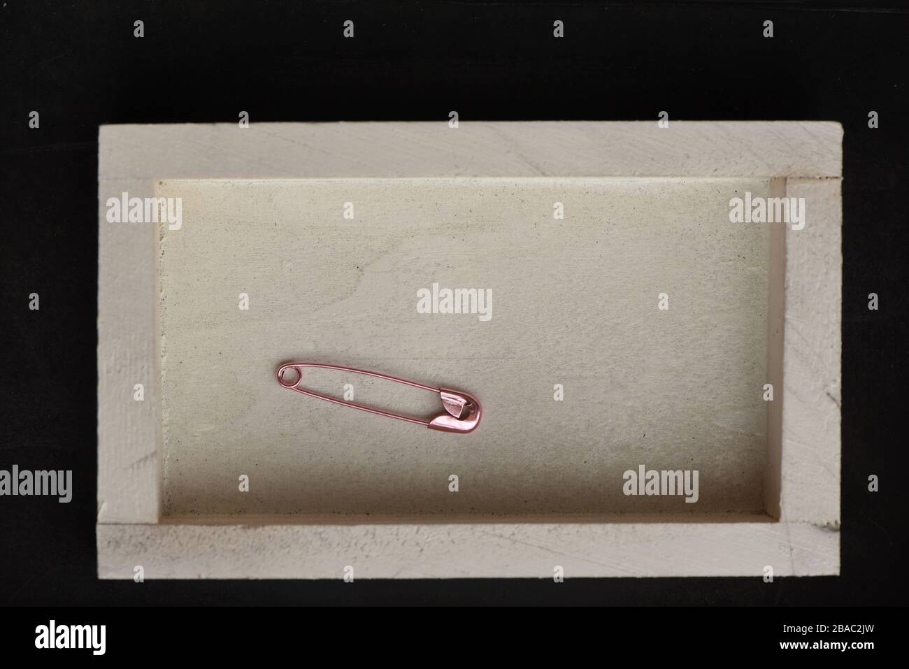 Vida útil que muestra un pasador de seguridad de pañal rosa en una caja de madera pintada en blanco Foto de stock