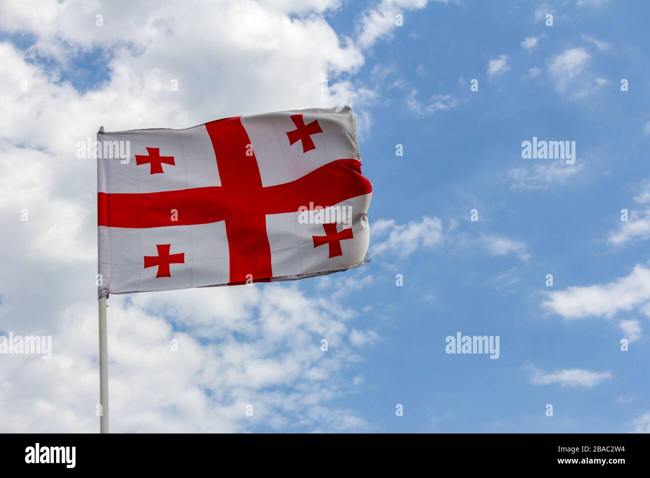 La bandera de la República de Georgia se asola en una fuerte brisa contra un cielo azul con nubes blancas Foto de stock