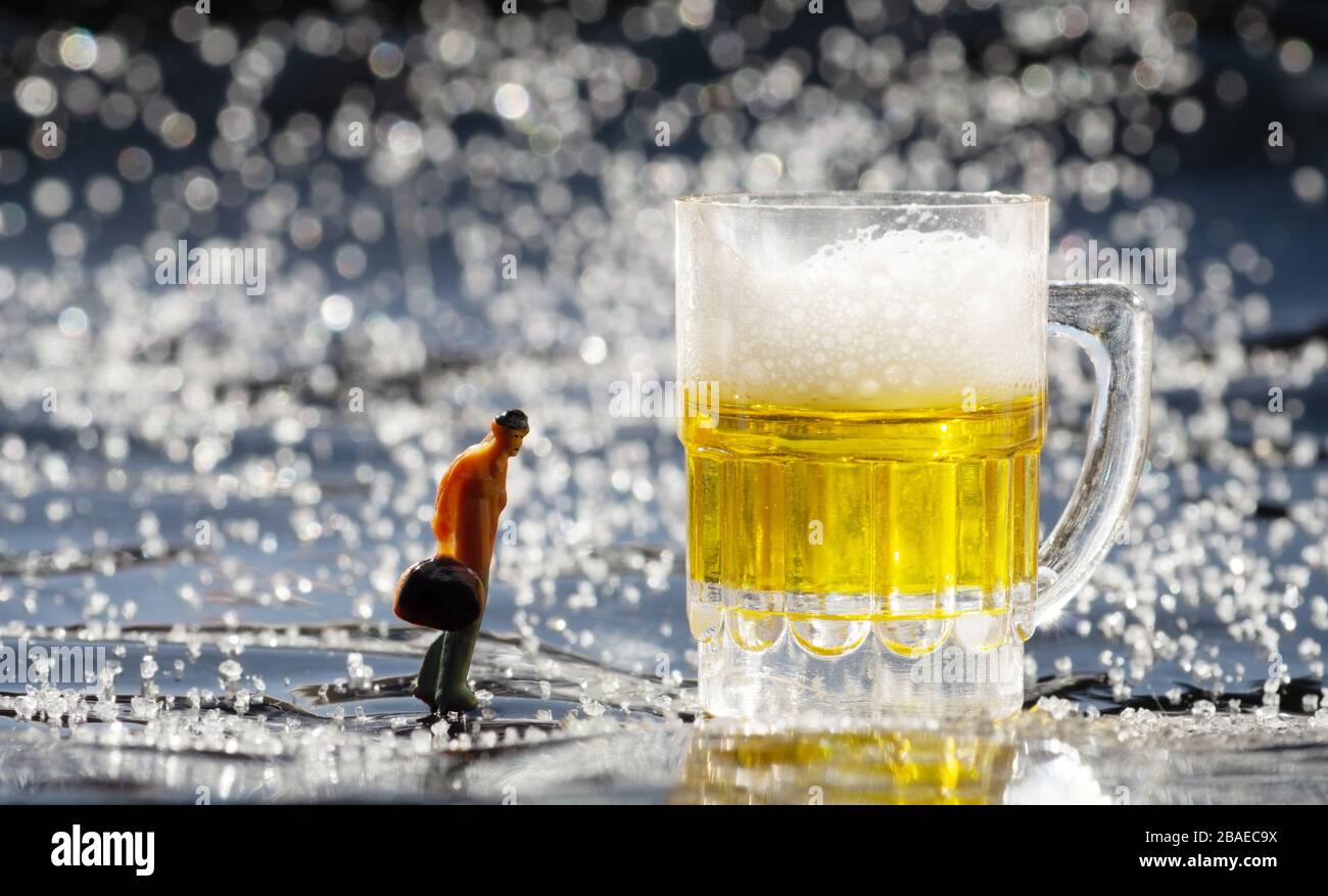 Una figura minúscula de una persona cerca de una taza pequeña de cerveza. Alcoholismo y problema de consumo moderado Foto de stock