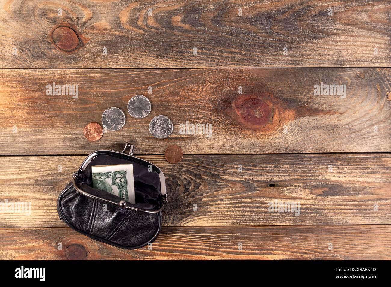 Cartera de bolsillo de cuero negro abierto con monedas de un céntimo, un cuarto de dólar y un billete de 2 dólares cerca. Crisis financiera, pobreza, falta de dinero. Sobre madera b Foto de stock