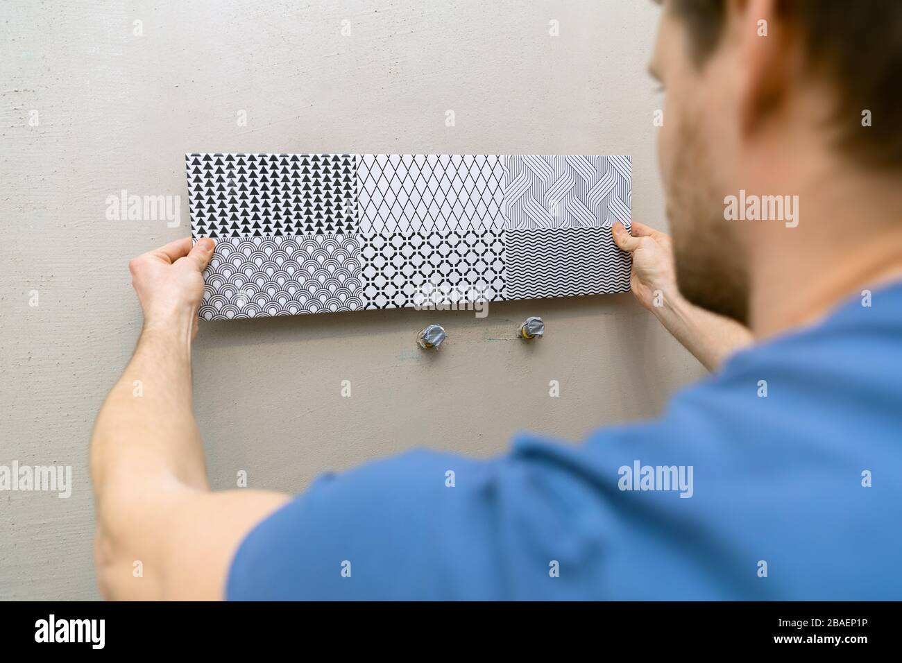 hombre intentando decoración de azulejos en la pared del baño Foto de stock