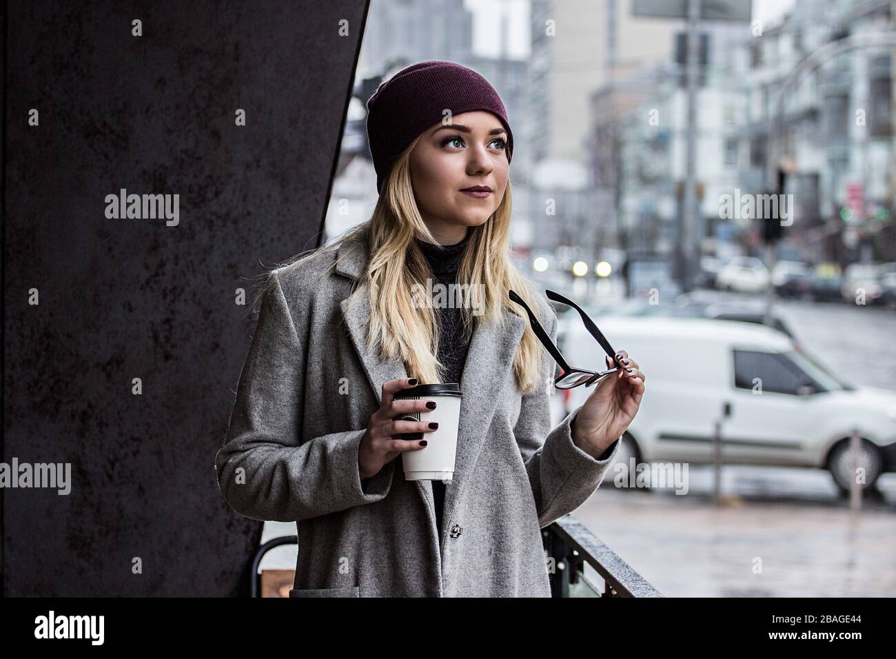 Mujer en ropa de invierno elegante con taza de café al aire libre.