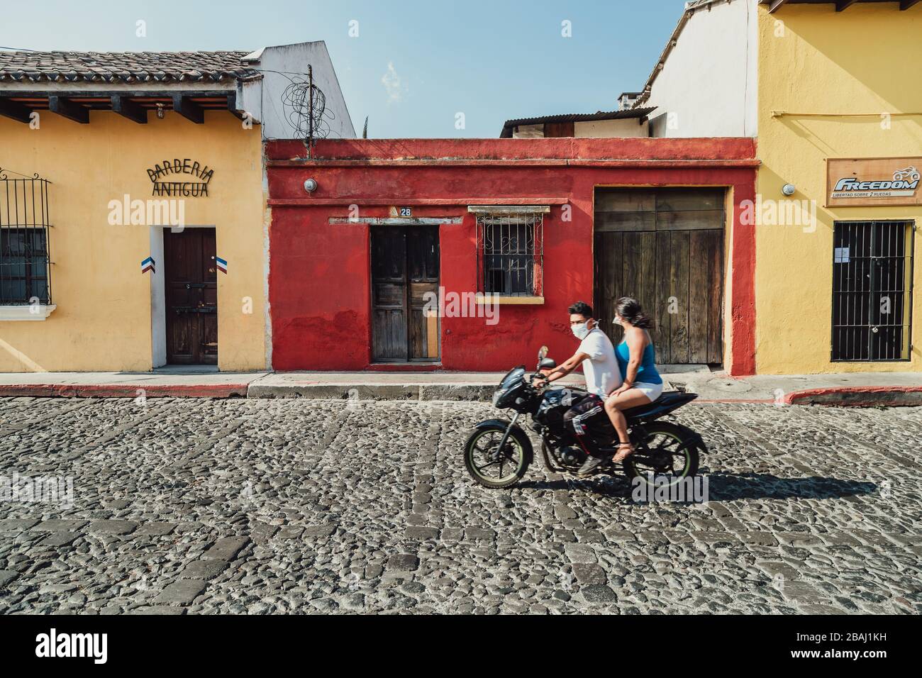 Pareja en su moto usando máscaras faciales durante la pandemia del coronavirus. Calles vacías en la colorida ciudad colonial de Antigua Guatemala Foto de stock