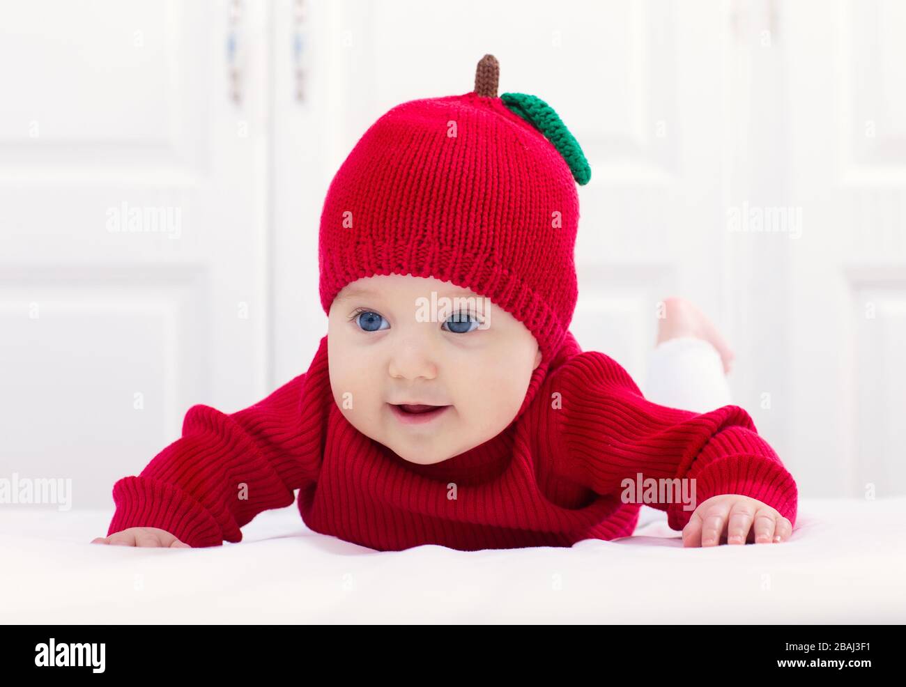 Bebé con gorro de manzana de punto. Niño en cama blanca. Niño que lleva  Jersey rojo de otoño en casa. Disfraz de Halloween o temporada de otoño  Fotografía de stock - Alamy