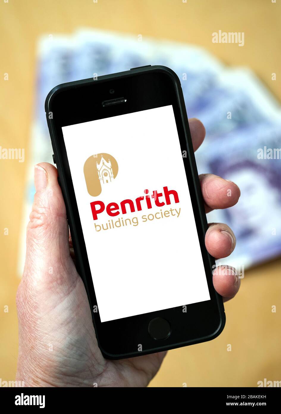 Una mujer que tiene un teléfono móvil mostrando Penrith Building Society (sólo para uso editorial) Foto de stock