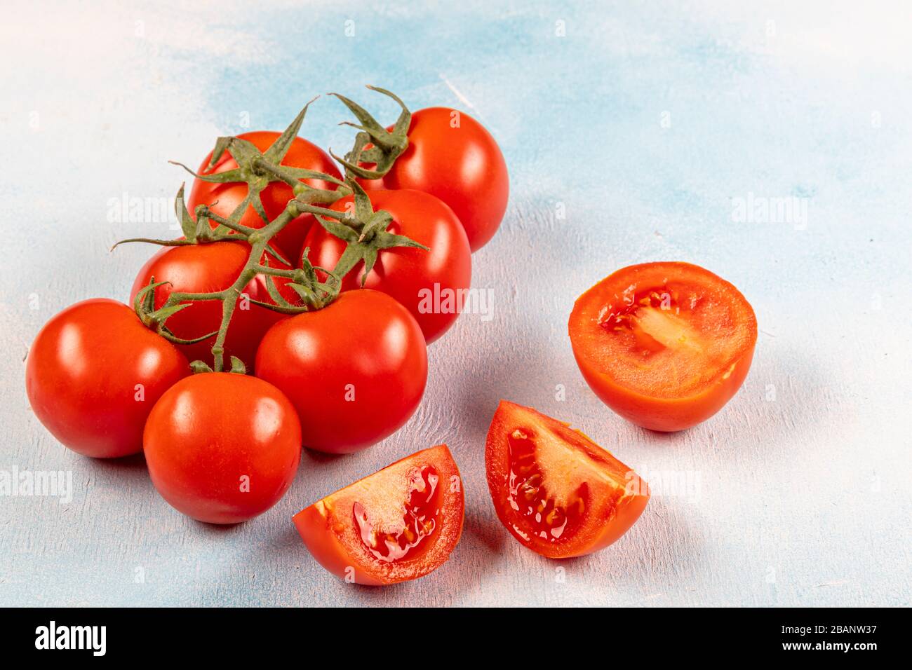 Tomates en rama (tomates de vid). Tomates sobre la vid y sobre un fondo de madera azul. Hermosos tomates con una hermosa rama verde. Foto de stock