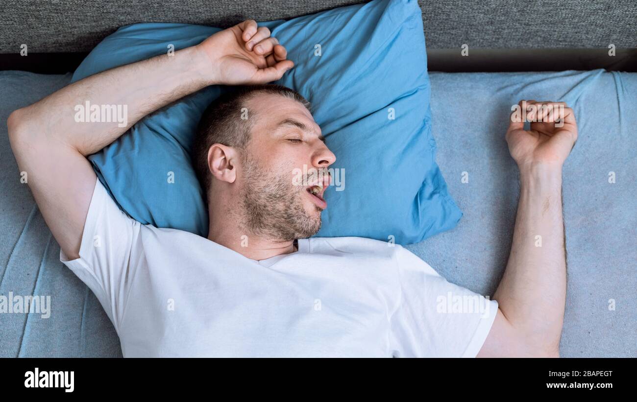 Hombre durmiendo en la cama en casa durante el auto-aislamiento pandémico, Panorama Foto de stock