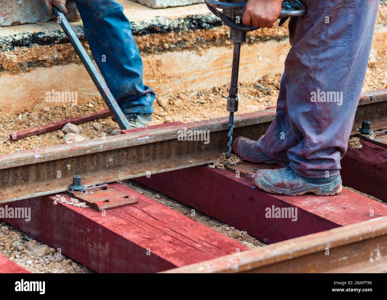 Trabajadores del ferrocarril que están atornillando el ferrocarril. Trabajador de detalle con máquina de perforación de traviesas portátiles Foto de stock