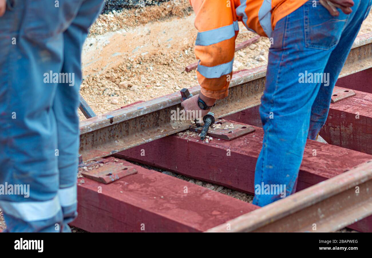 Trabajadores del ferrocarril que están atornillando el ferrocarril. Trabajador de detalle con llave de apriete mecánica Foto de stock