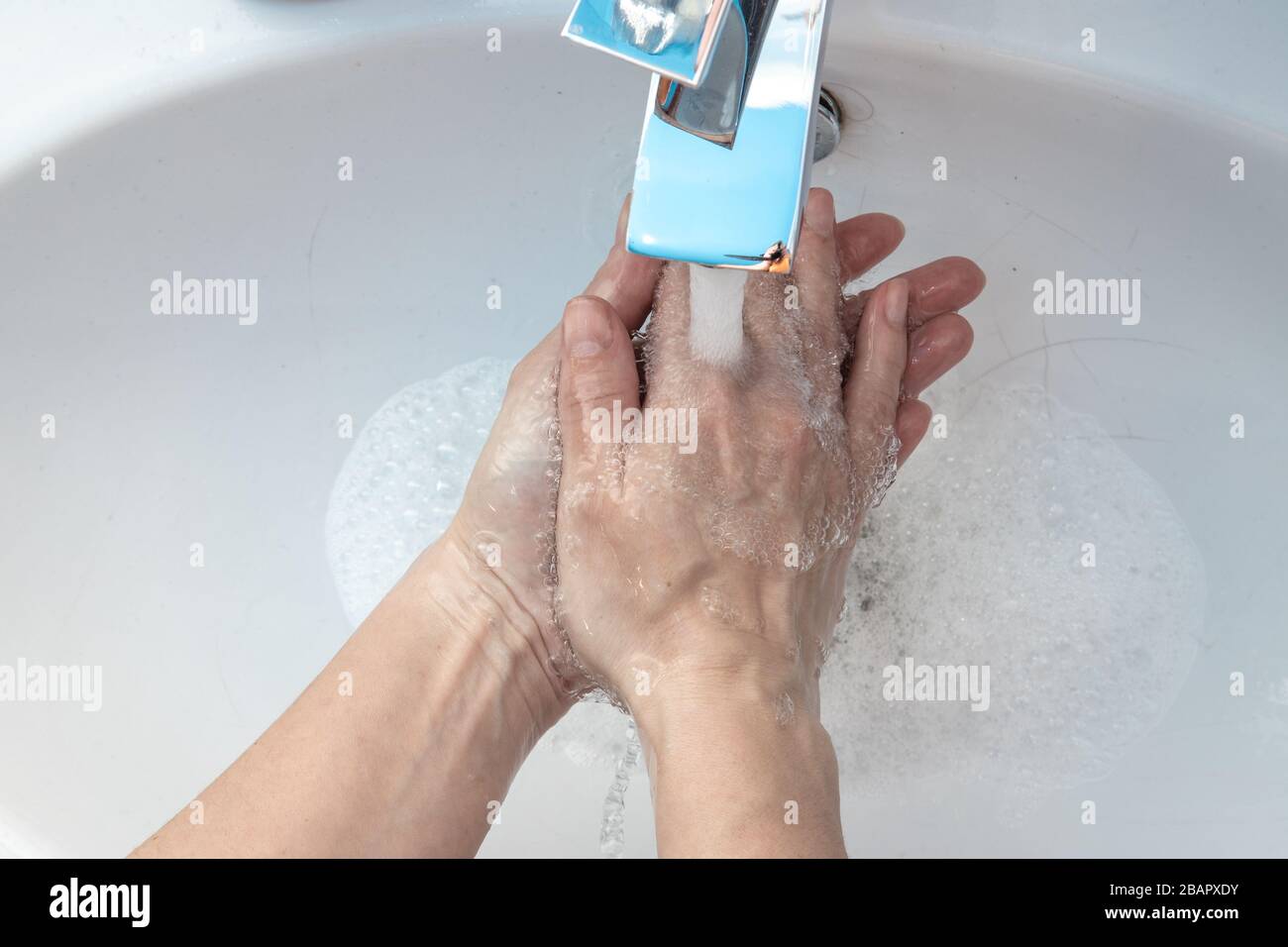 Arriba cerca arriba ver a la mujer de pie en el cuarto de baño lavándose las manos bajo el agua que fluye enjuagando el jabón. Detenga el virus de corona covid19, mantenga la higiene personal Foto de stock