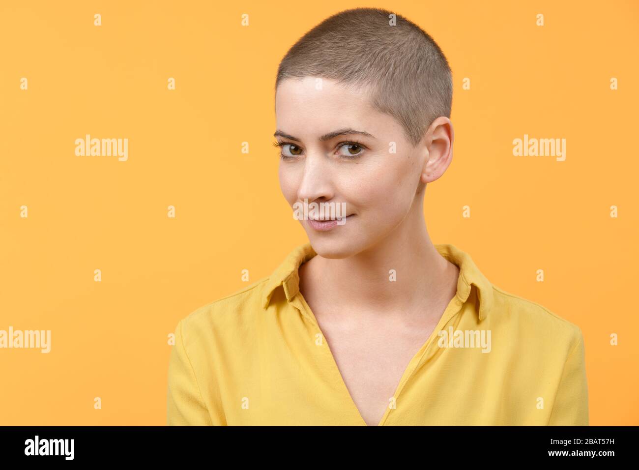 Retrato de estudio de una hermosa mujer caucásica joven con cabeza afeitada sobre fondo amarillo brillante. Retrato de sobreviviente de cáncer. Foto de stock