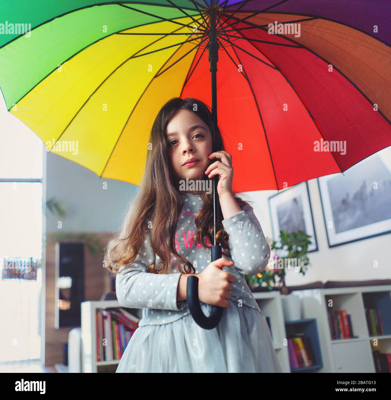 Retrato de una miserable niña que sostiene un paraguas colorido dentro de la casa Foto de stock