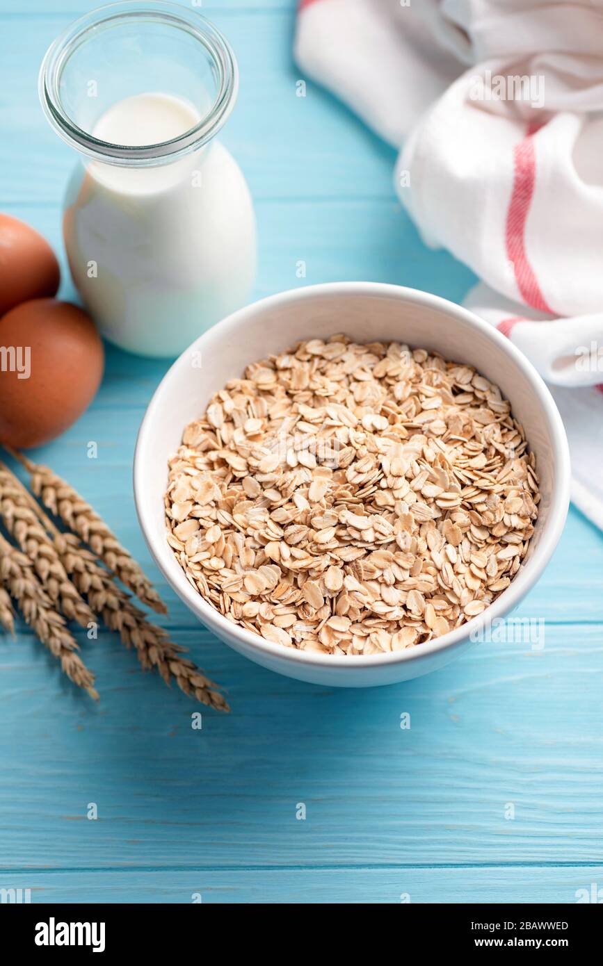 Copos de avena y botella de leche sobre fondo de mesa de madera azul. Ingredientes para cocinar avena o galletas de avena saludables Foto de stock