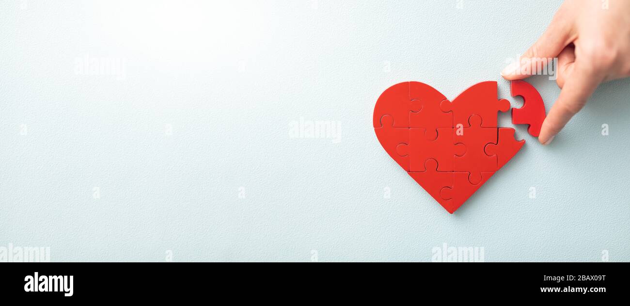 El concepto de caridad, amor, donación y ayuda. Día internacional de la cardiología. Una mujer organiza rompecabezas de forma de corazón rojo. Símbolo de ayudar a otros Foto de stock