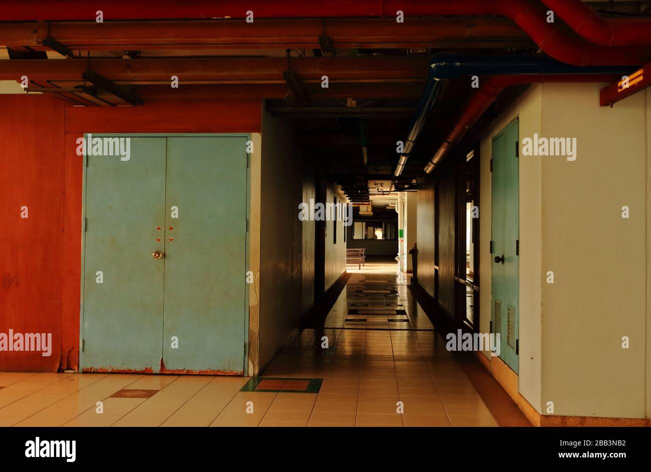 Pasillo silencioso en un edificio al lado de la puerta de madera azul en descomposición, con tuberías de agua roja instaladas en el techo Foto de stock