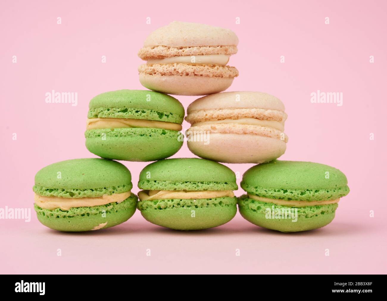 pila de pasteles redondos blancos y verdes de harina de almendras macarons con crema sobre fondo rosa, deliciosa tarta. Foto de stock