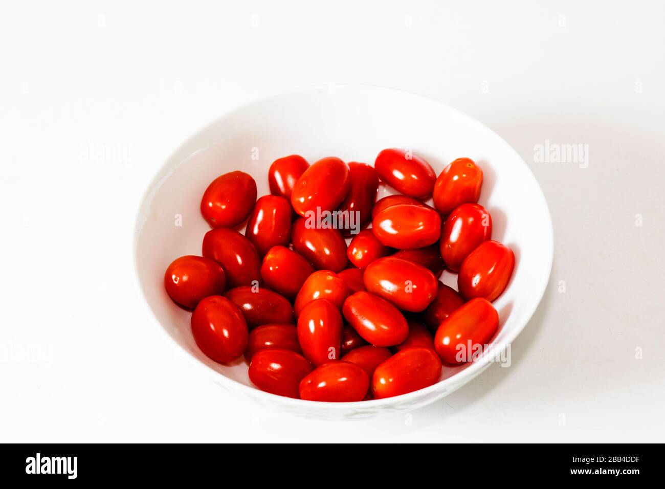 Un tazón blanco lleno de deliciosos tomates ciruelos, mezclados juntos. Con fondo blanco. Un aperitivo orgánico y saludable, vegano y lleno de vitaminas. Foto de stock