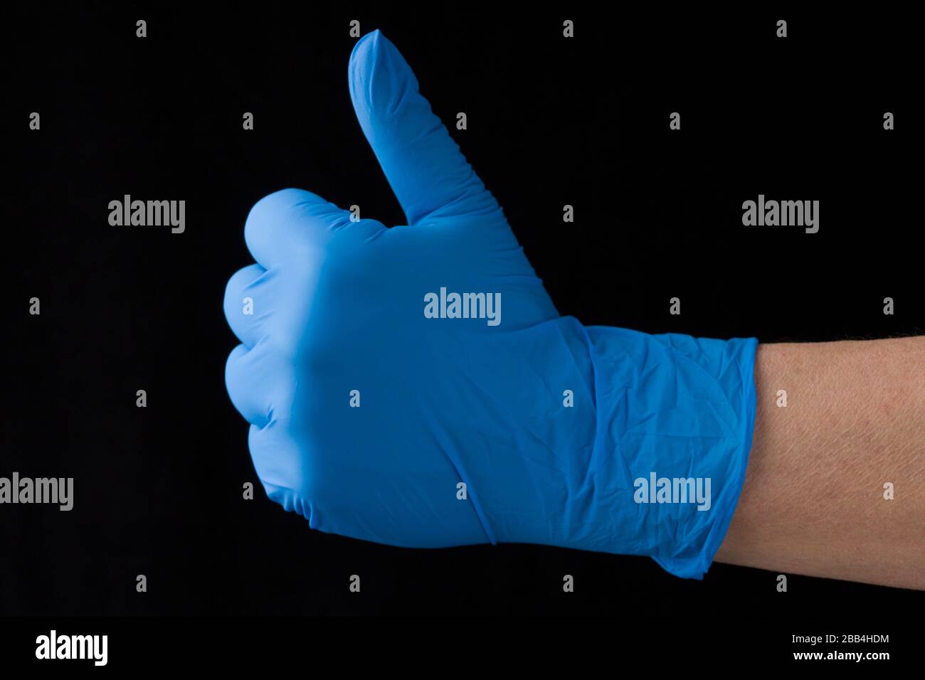 Mano mostrando el pulgar hacia arriba en un guante médico azul aislado sobre fondo negro. Foto de stock