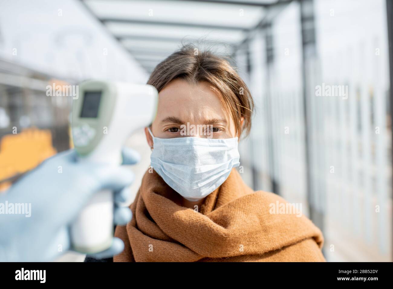 Medición de la temperatura con termómetro infrarrojo de una mujer joven en máscara facial en un punto de control durante una epidemia al aire libre. Concepto de prevención la propagación del virus Foto de stock