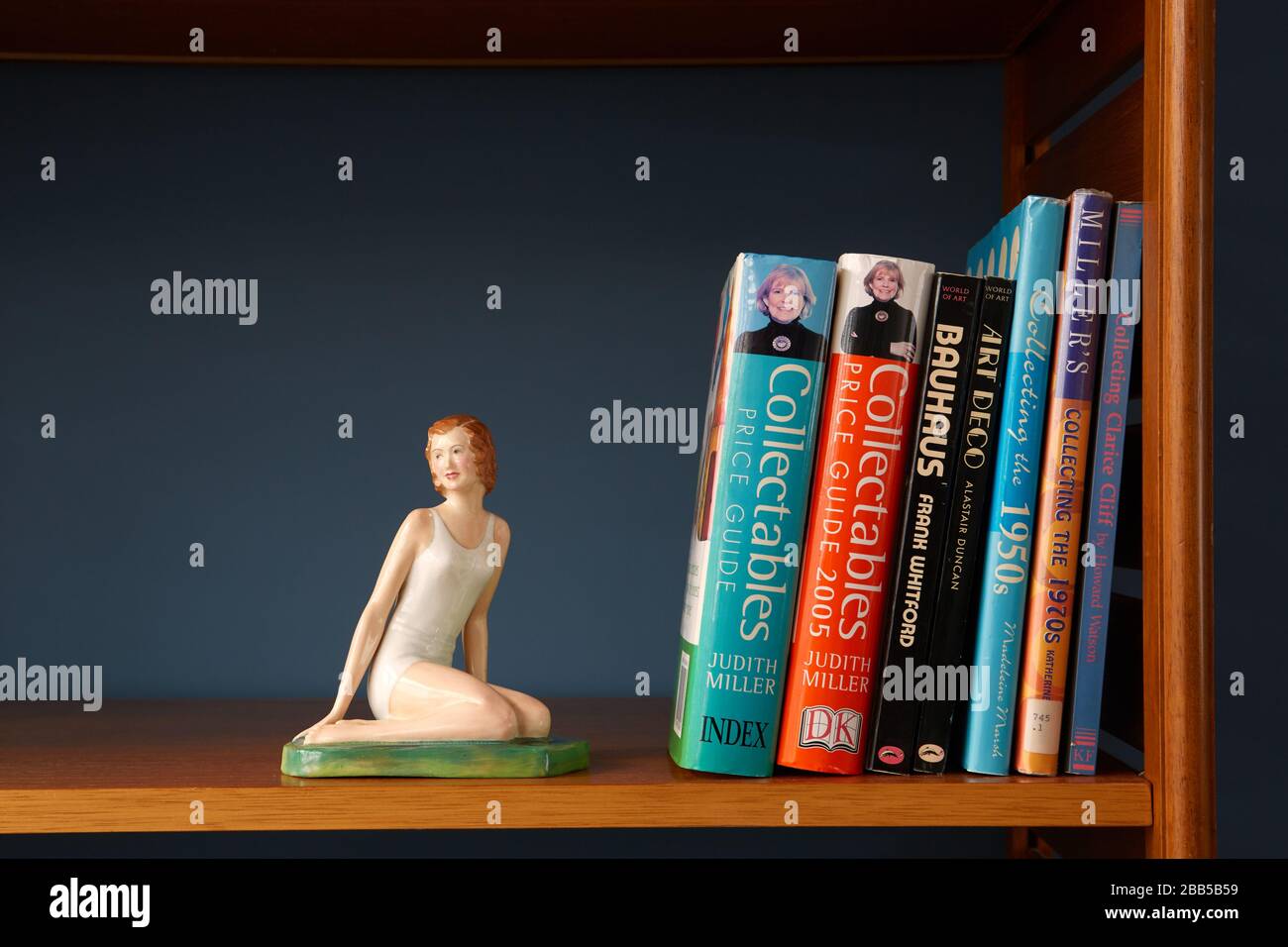 Fotografía de una figurilla de porcelana de mujer arrodillada en un estante, junto con libros sobre coleccionables y arte Foto de stock