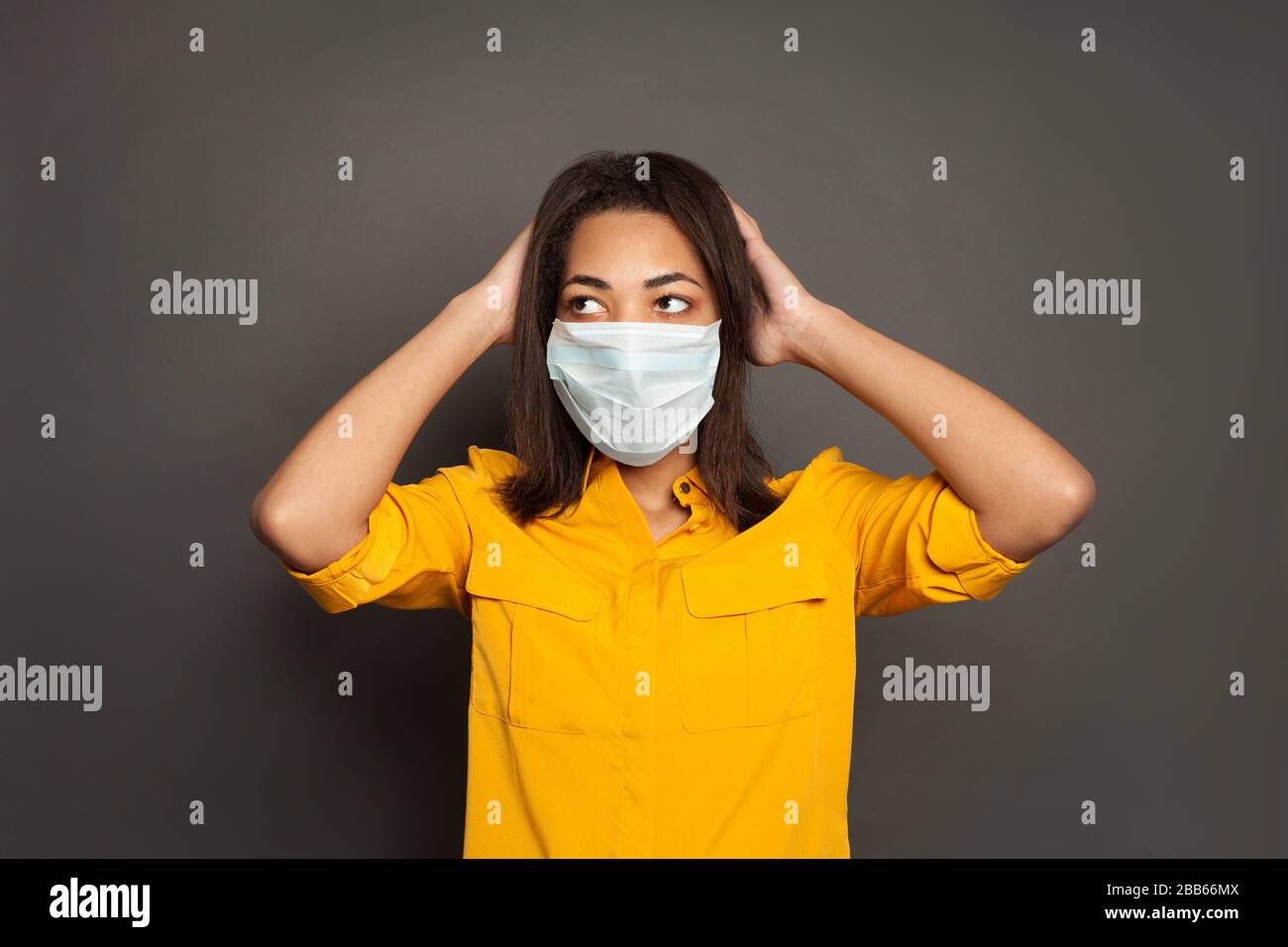 Concepto de protección contra epidemias y virus. Mujer afroamericana en pánico en máscara de cara sobre gris Foto de stock