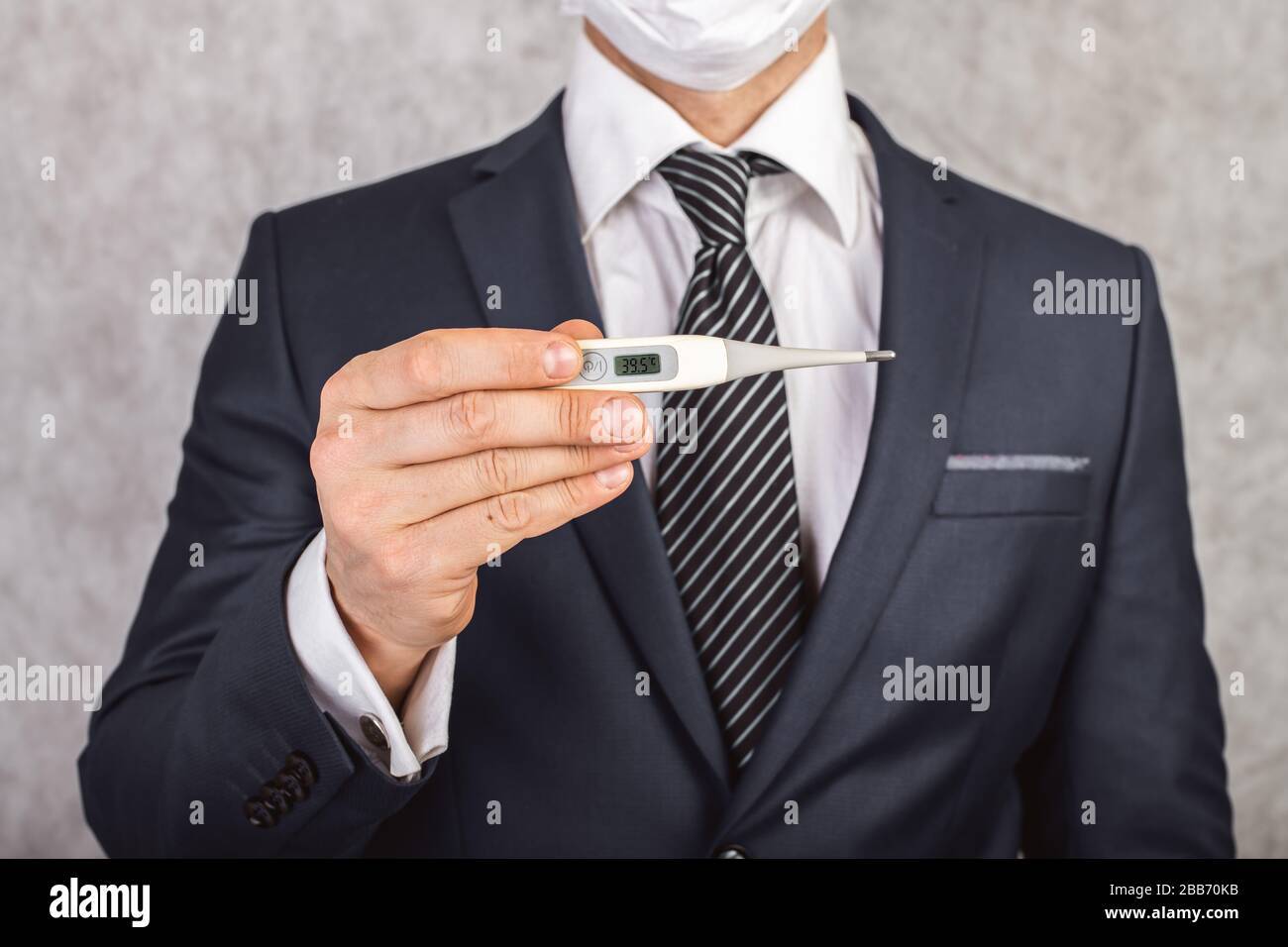 Un hombre en un traje y corbata sostiene en sus manos un termómetro electrónico con temperatura de 39.5 Foto de stock