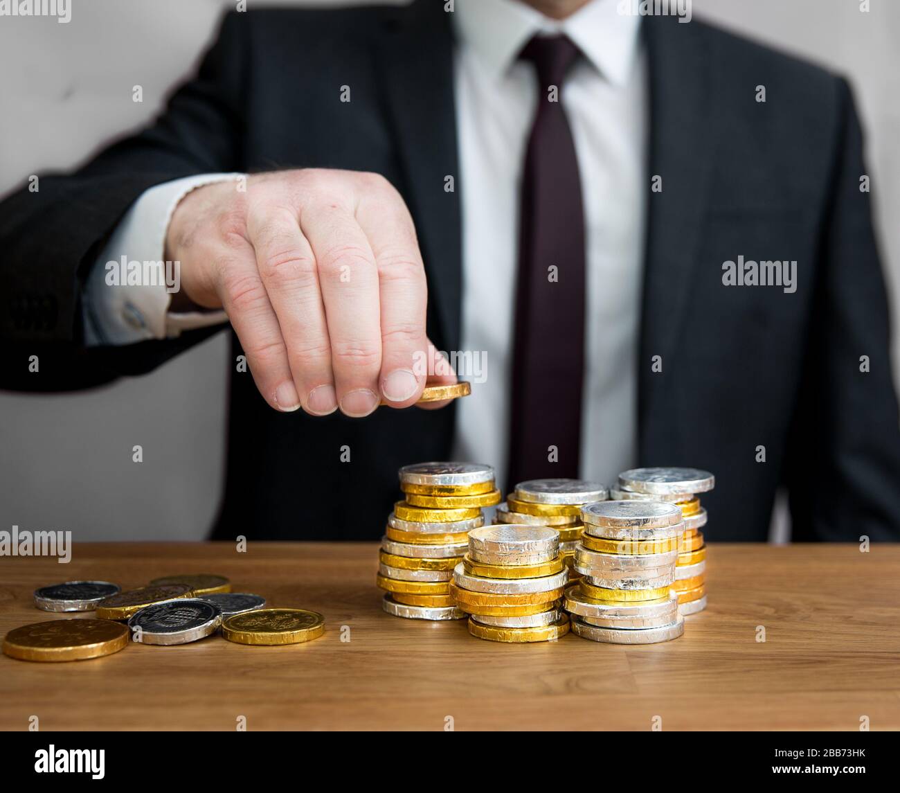 Un concepto de sección media de un hombre de negocios con una gran cantidad de monedas de recuento en efectivo en pilas para sumar beneficios y activos corporativos. Foto de stock