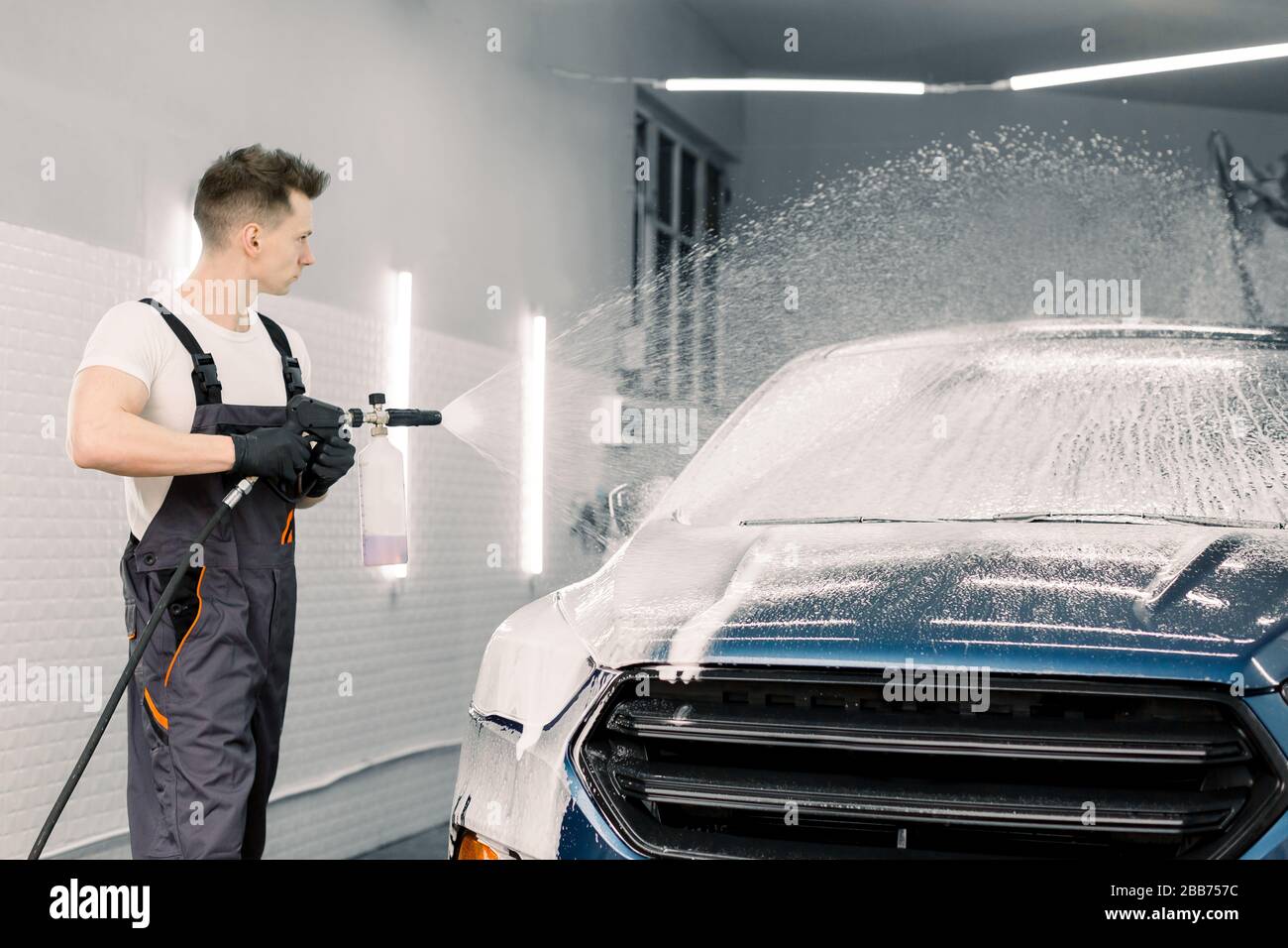 Un hombre apunta un pulverizador de espuma a un coche un coche en un lavado  de coches de autoservicio