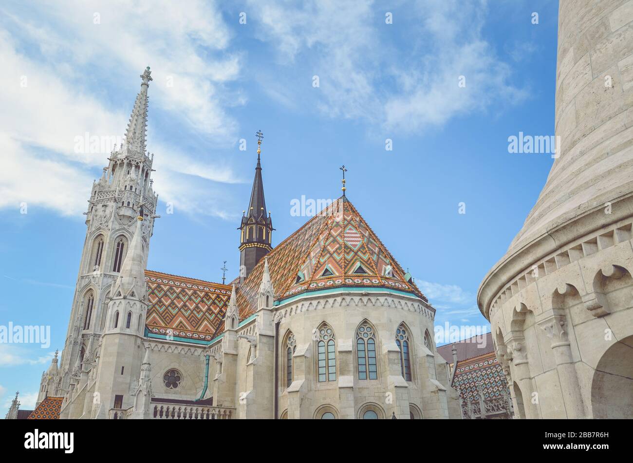 La aguja de la famosa iglesia Matthias en Budapest, Hungría. Iglesia Católica Romana construida en estilo gótico. Techo de baldosas de color naranja. Cielo azul y nubes blancas arriba. Foto horizontal con filtro. Foto de stock