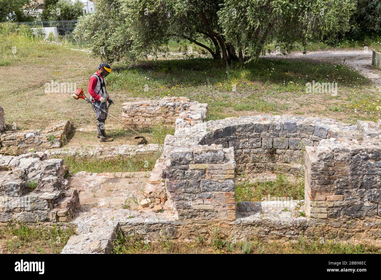 Wokman desbrotando malezas en las ruinas romanas de Milreu, Algarve, Portugal Foto de stock
