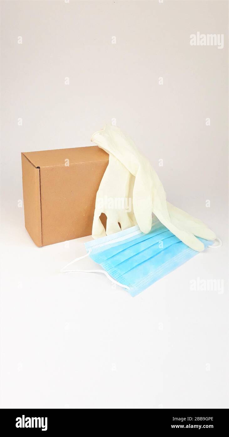 Caja de cartón marrón, guantes médicos blancos de látex y máscara médica azul sobre un fondo blanco, copia spaes.entrega segura de pedidos en línea durante el Foto de stock