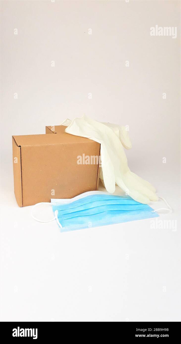 Caja de cartón marrón, guantes médicos blancos de látex y máscara médica azul sobre un fondo blanco, copia spaes.entrega segura de pedidos en línea durante el Foto de stock