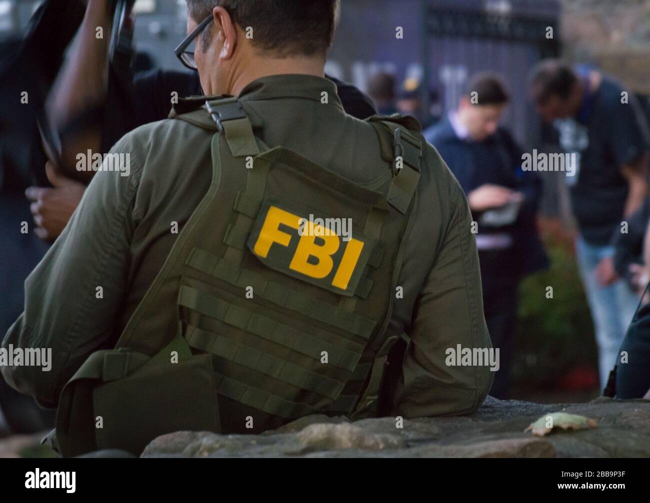Agente del FBI, varón caucásico, con gafas en un chaleco verde a prueba de  balas con el logotipo del FBI visto desde atrás en el lugar de  investigación Fotografía de stock -