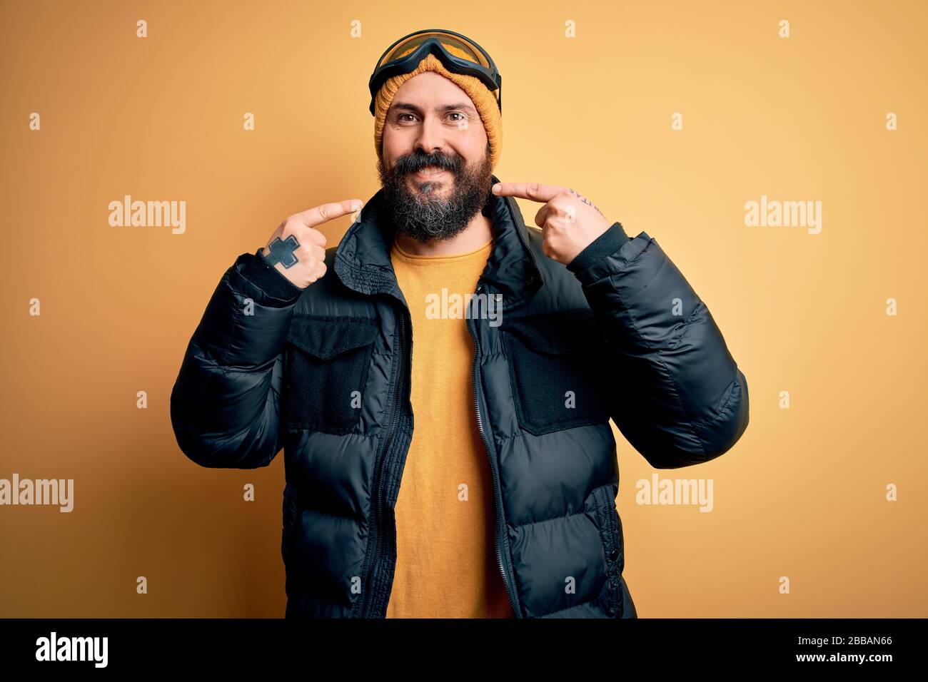 hombre calvo muy bonito esquiador barba esquiando usando ropa deportiva de nieve y gafas de esquí sonriendo alegre mostrando y señalando con dedos dientes y la boca de