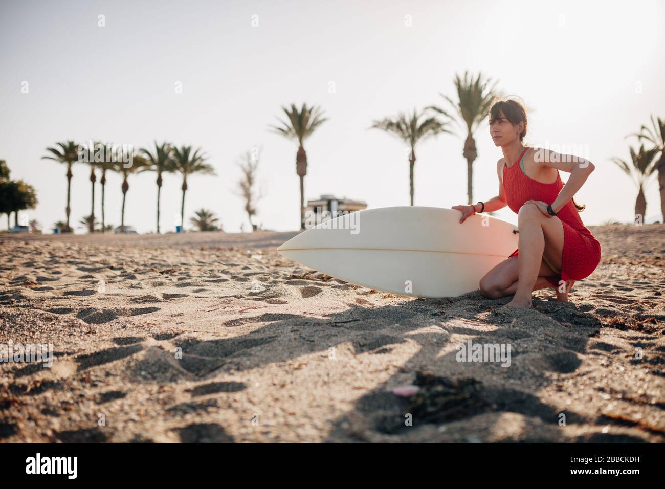 Mujer joven en la playa con su mesa de surf esperando en la arena Foto de stock