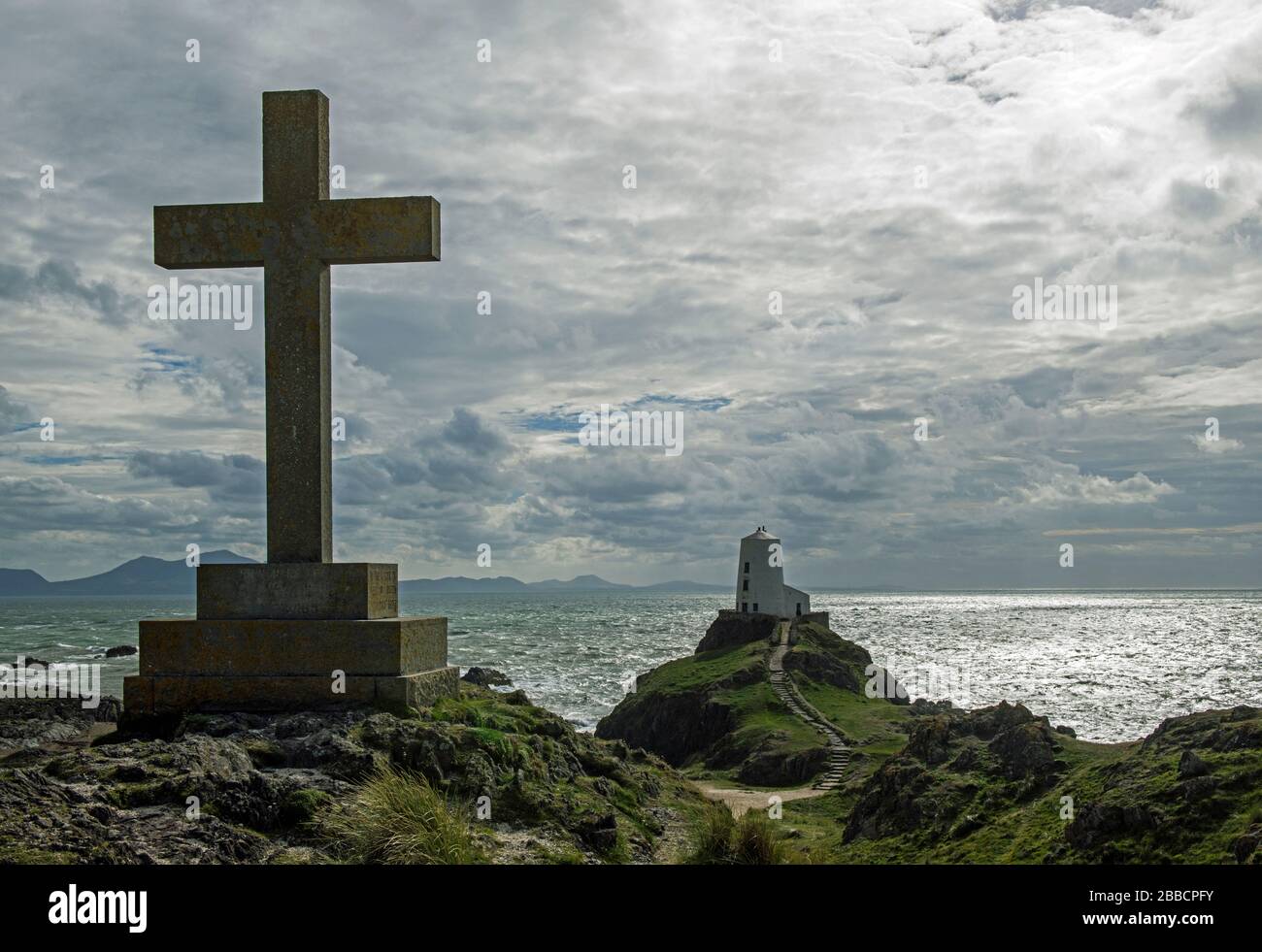 Isla Llanddwyn frente a la costa de Anglesey. Esto muestra una de las varias cruces en la isla junto con el faro de Ty Mawr con una puesta de sol de plata Foto de stock