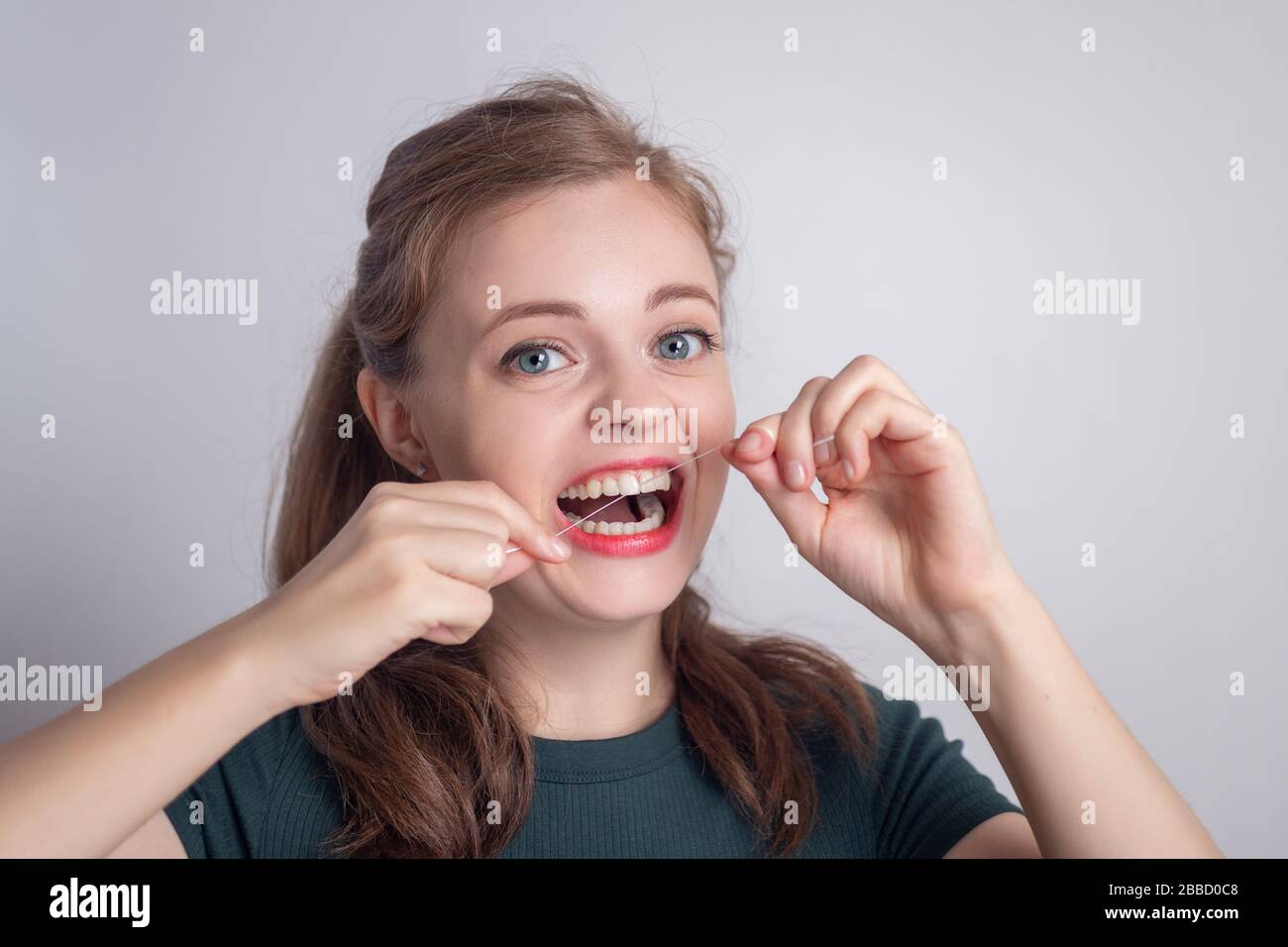 Chica joven caucásica sonriente divertida usando hilo dental Foto de stock