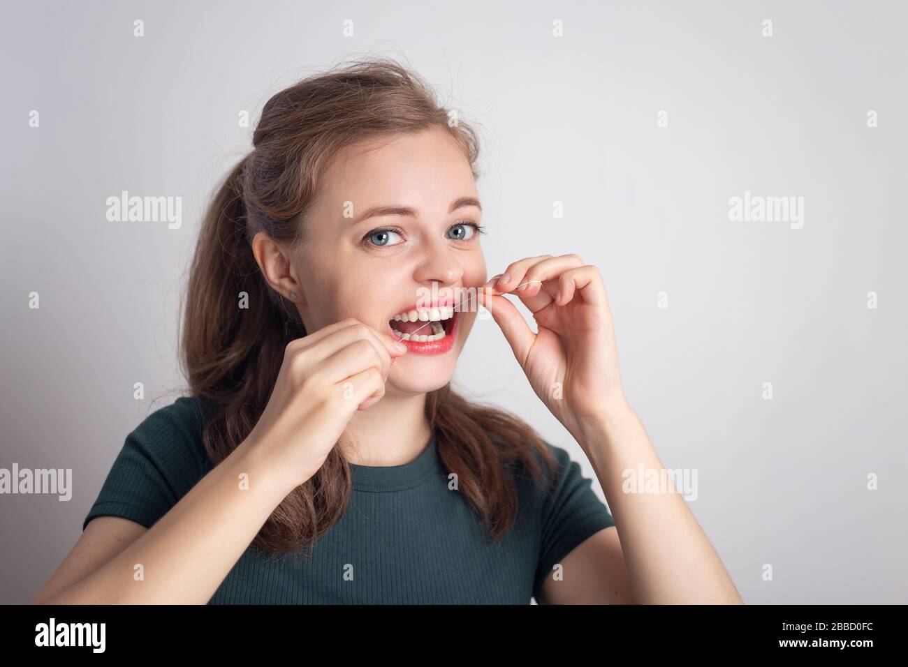 Chica joven caucásica sonriente divertida usando hilo dental Foto de stock