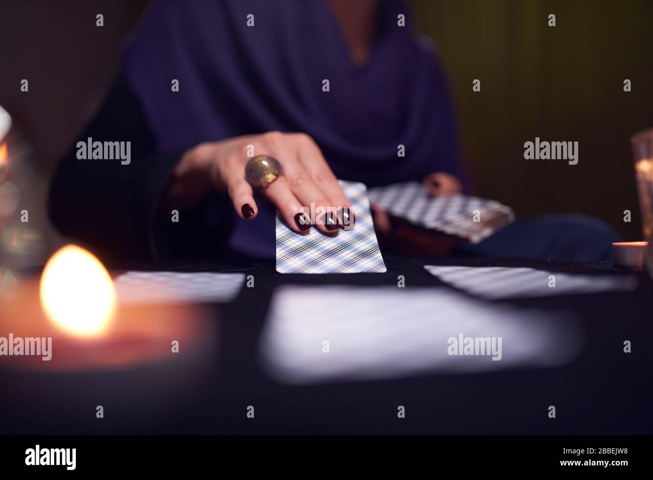 Primer plano de las manos de la mujer mitt-Reader con tarjetas de adivinación en la mesa con velas en la habitación oscura Foto de stock
