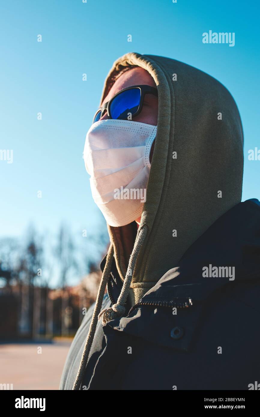 Hombre joven en la capucha con mascarilla facial para evitar la infección por virus y prevenir la propagación de la enfermedad. A pie en el centro de la ciudad. Infección por virus pro Foto de stock