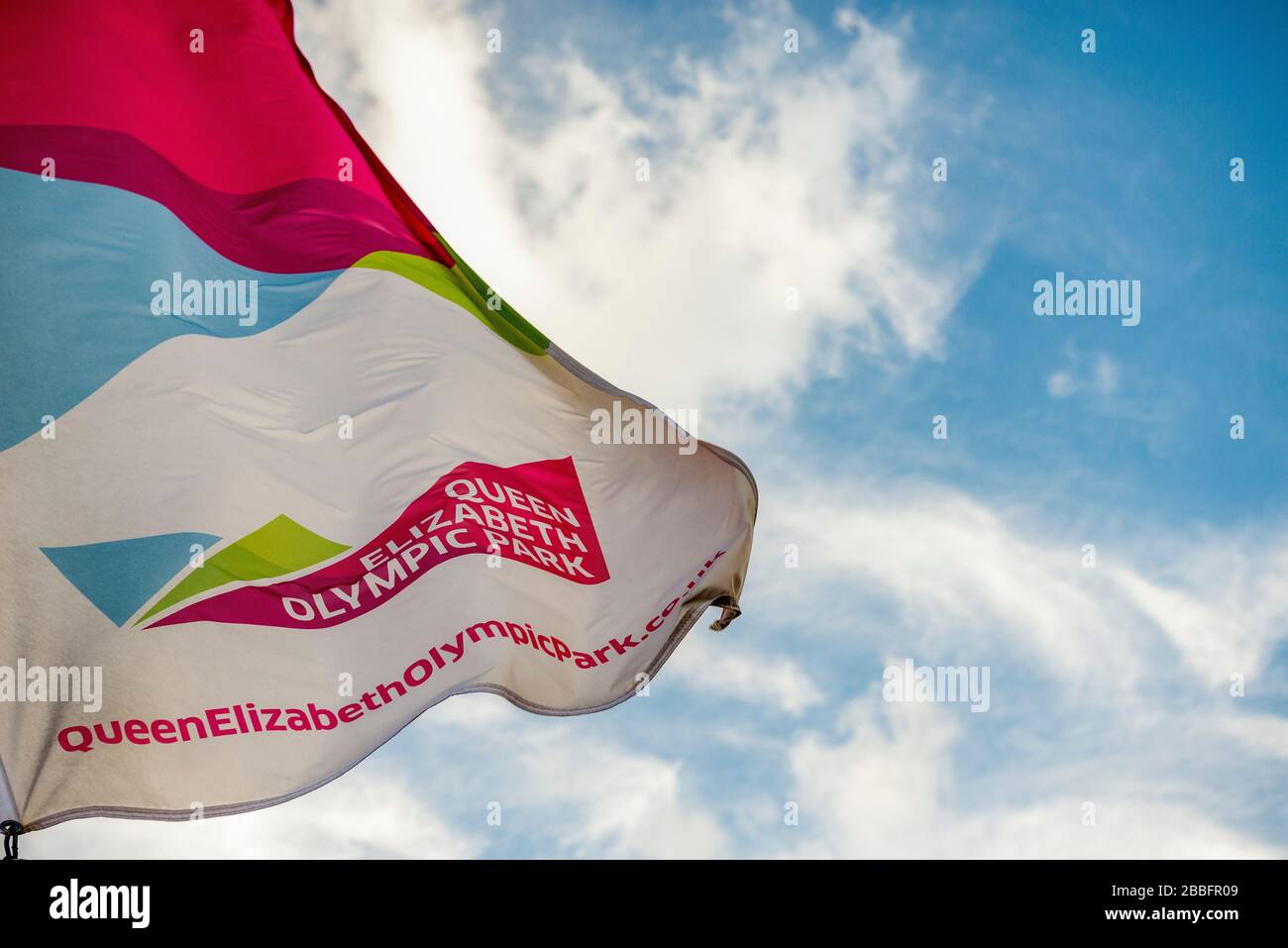 Una bandera con el logotipo y los colores del Parque Olímpico Reina Isabel en un día soleado y claro en el este de Londres Foto de stock