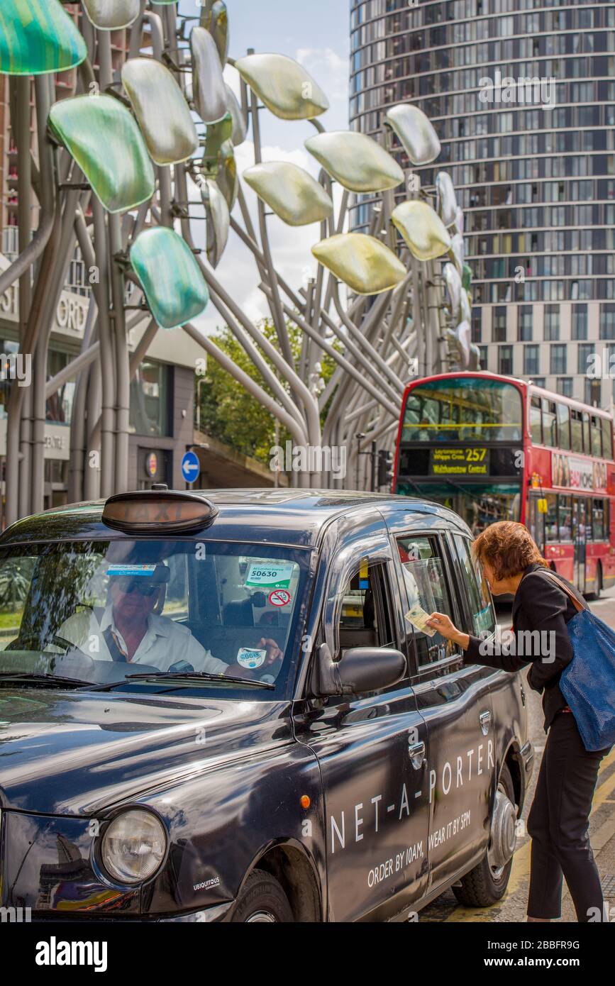 Una mujer que paga dinero en efectivo a un taxista negro de Londres para su viaje al centro comercial Stratford en el este de Londres Foto de stock